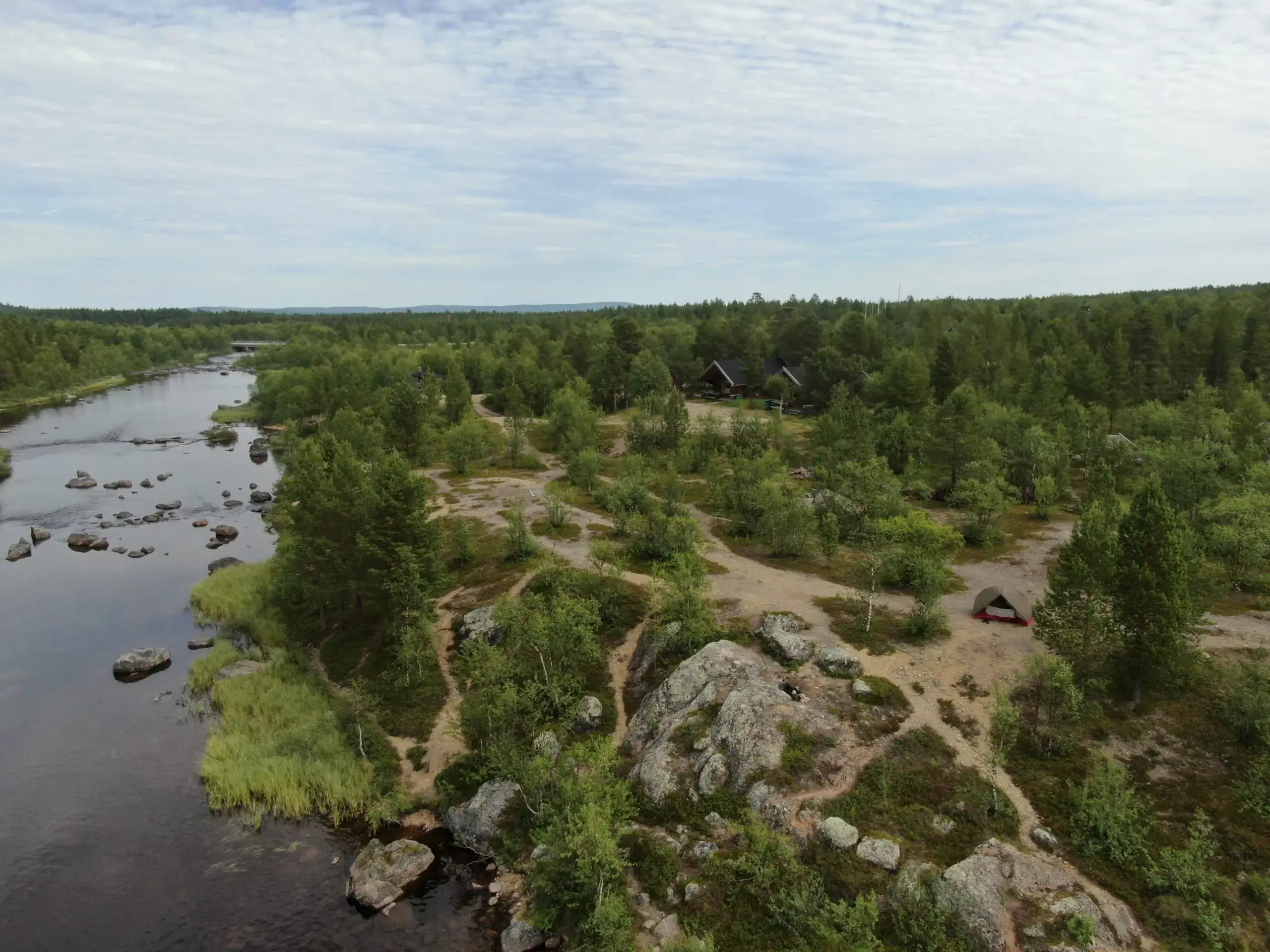 Aerial view of the Muotkan Ruoktu cabins among pines, beside the Peltojoki river
