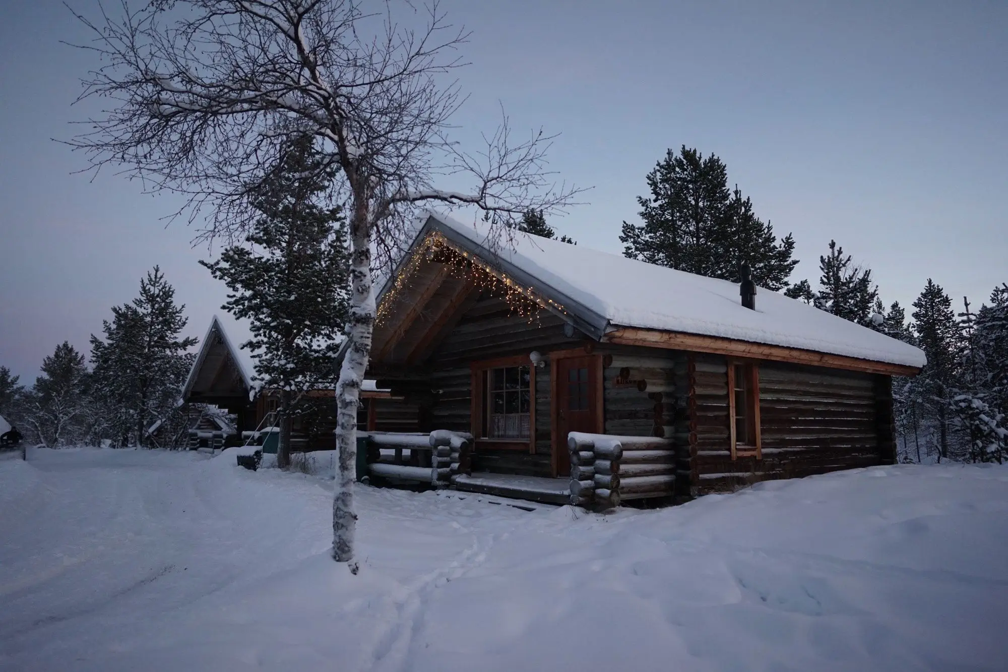 A log lodge with snow on its roof, lit up at dusk on a winter evening