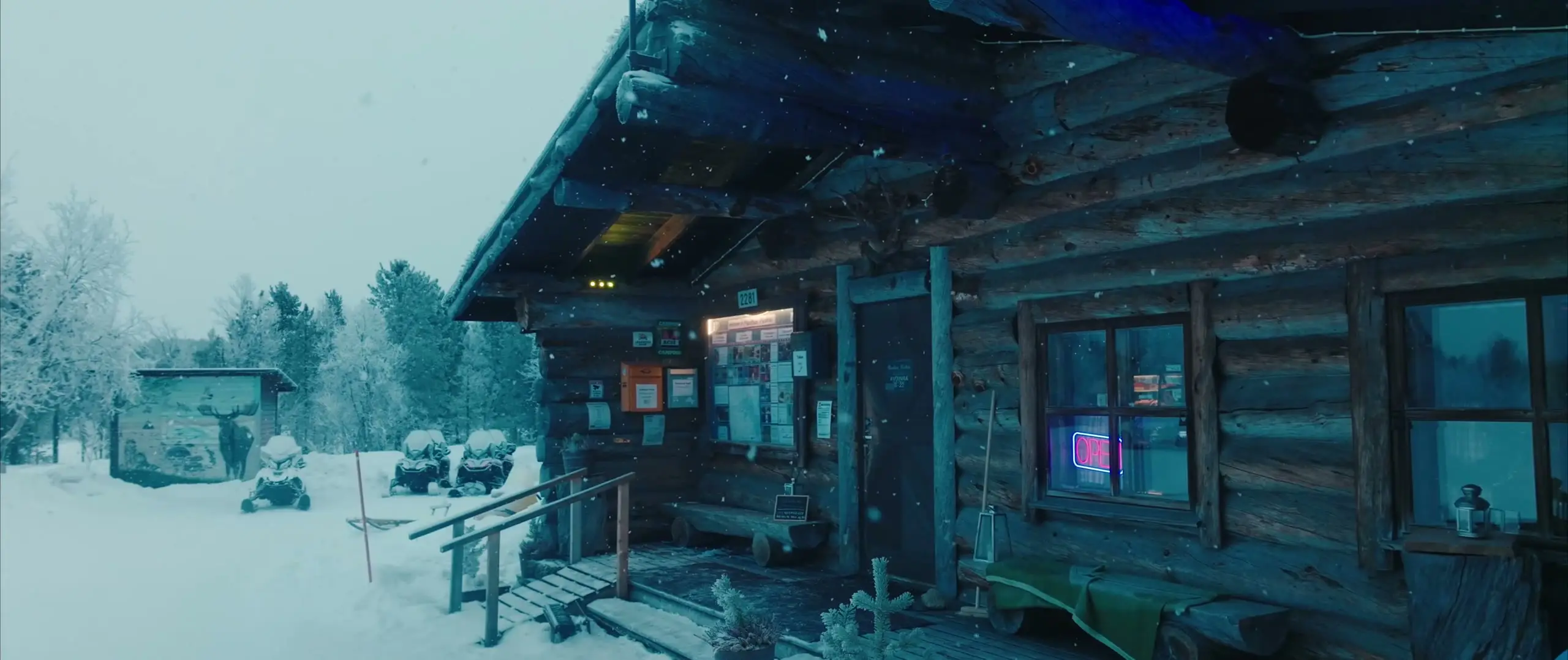 The log restaurant in falling snow, an Open sign glowing in the window and snowmobiles parked outside