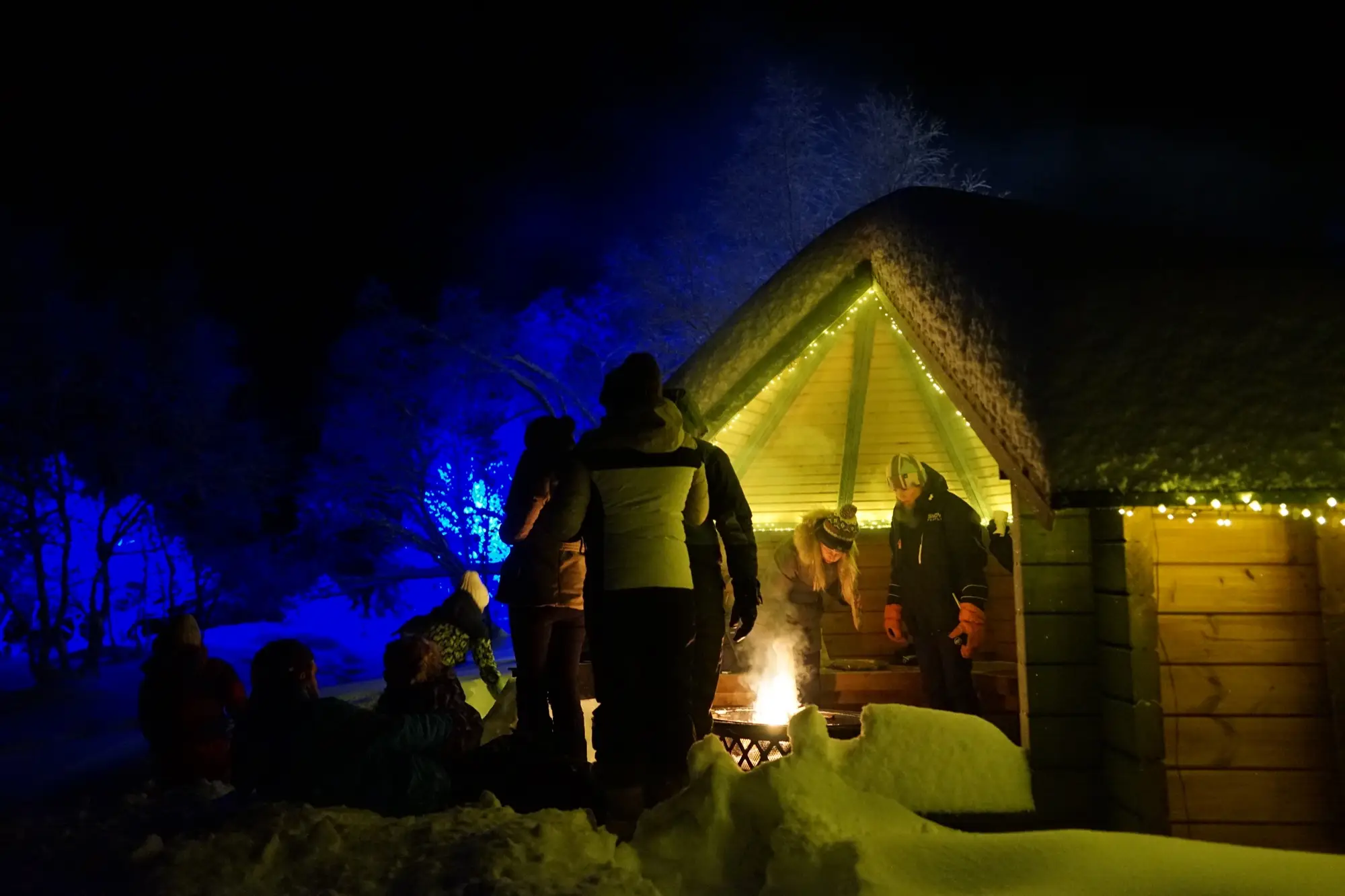 Guests gathered round the fire outside a snowy kota lit with fairy lights